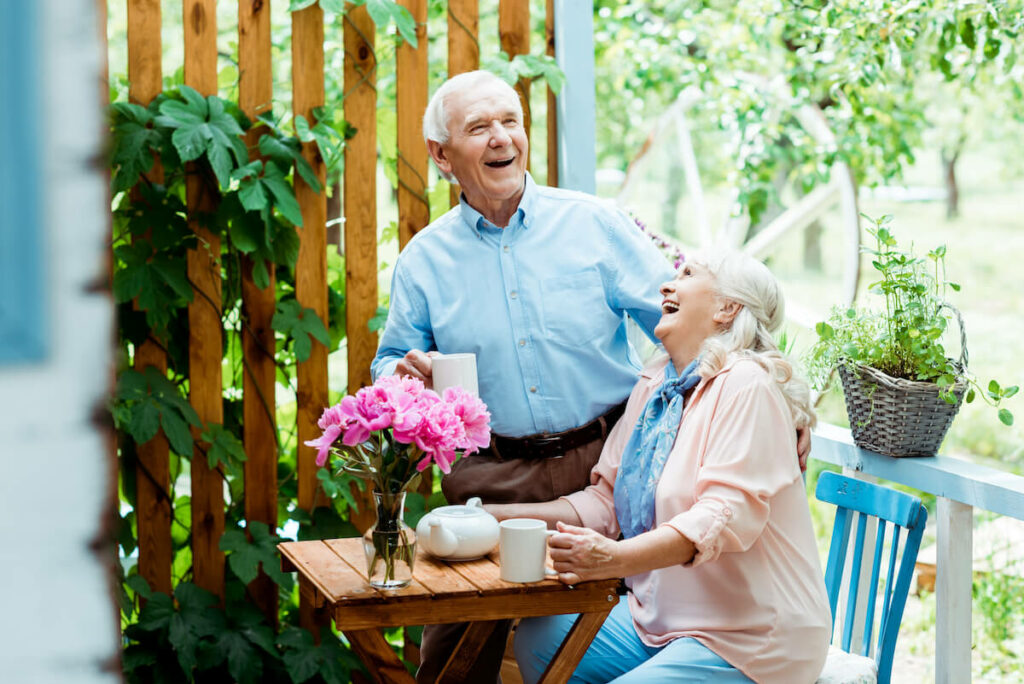 The Landing at Queensbury | Senior couple laughing over a cup of tea surrounded by flowers