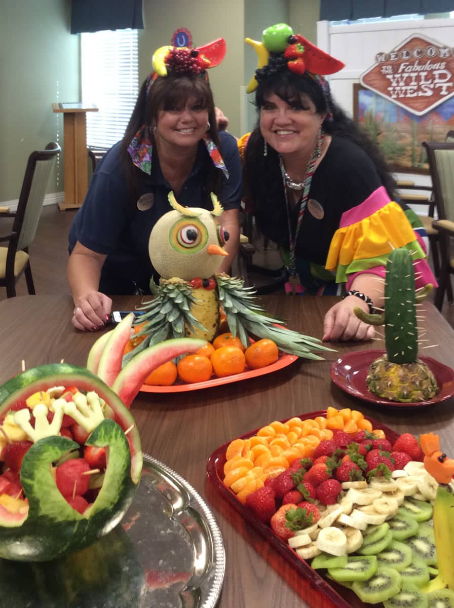 Pegasus Landing of Mesa | Teresa Hadley smiling with her coworker behind sculpted fruit