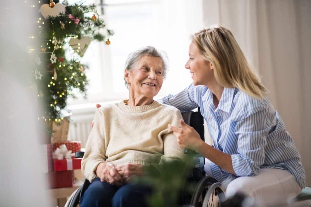 Broadway Mesa Village | Smiling senior woman with caregiver sitting beside the Christmas tree