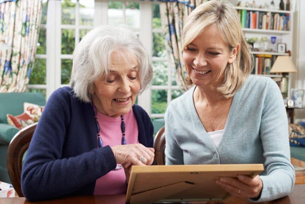 Broadway Mesa Village | Senior woman looking at photos with caregiver at table