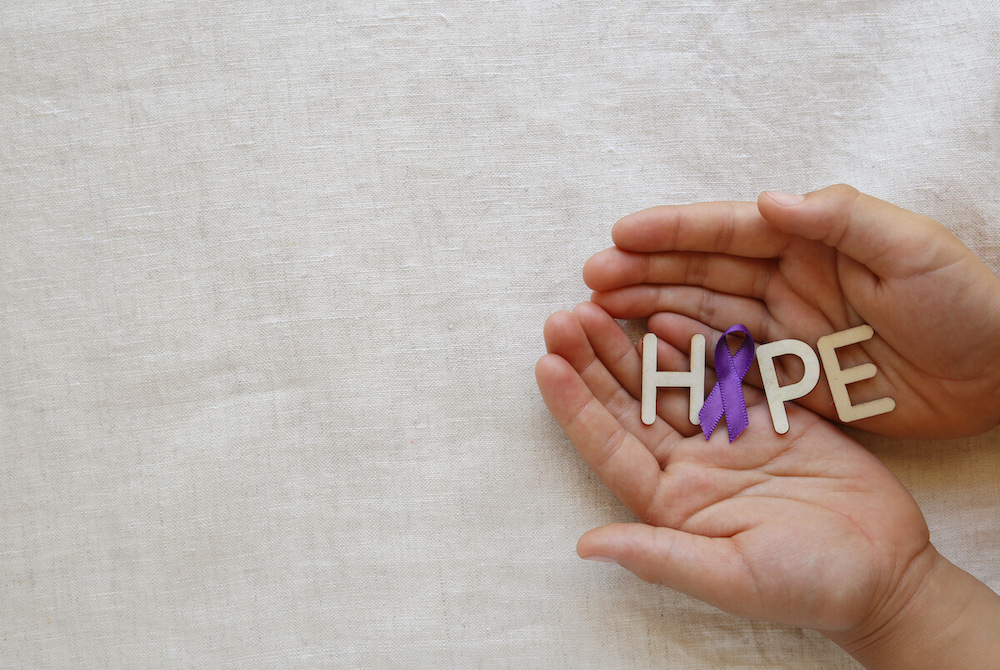 Pegasus Senior Living | Hands holding lettings spelling out hope, with a purper ribbon for the