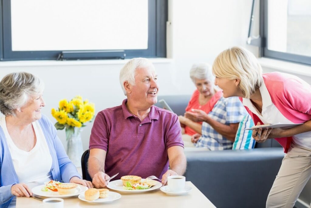 Cordata Court | Senior-couple enjoying a meal and getting checked on by a caregiver