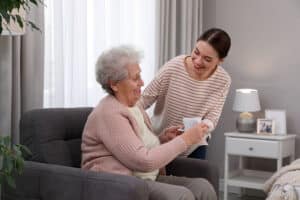 Glenwood Village of Overland Park | Young caregiver giving tea to senior woman in room.