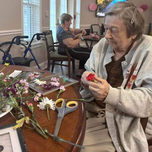 Glenwood Village of Overland Park | Senior woman creating floral craft in room of other crafters