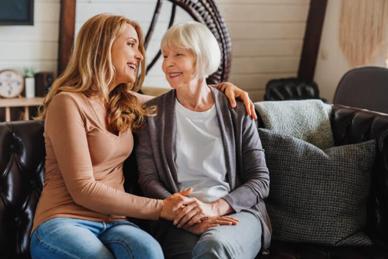 Magnolia Place of Roswell | Senior mother with adult daughter hugging each other on sofa in living room