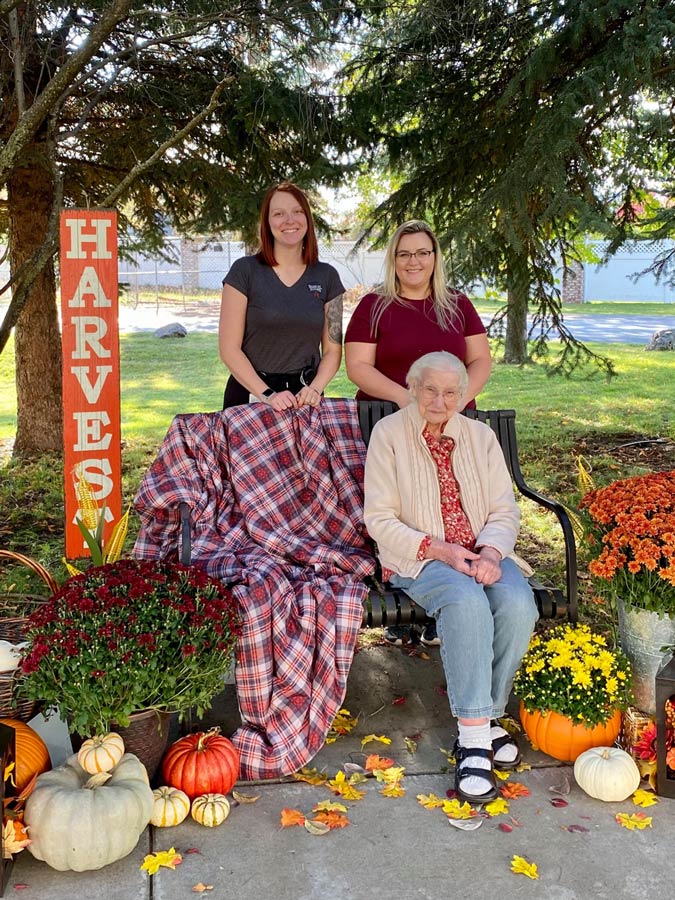 North Point Village | Senior woman sitting on bench in front of caregivers surrounded by autumn decorations