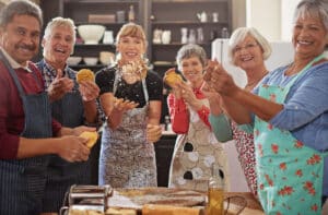 Pegasus Landing of Katy | A group of older adults in a baking class with their instructor, each holding dough, smiling and looking directly at the camera