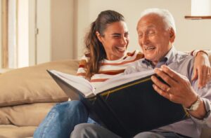 Pegasus Landing of Katy | An older adult man and his daughter smiling while looking at a photo album together.