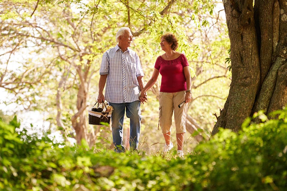 The Courtyards at Mountain View | Old couple, elderly man and woman in park walking in forest with picnic basket.