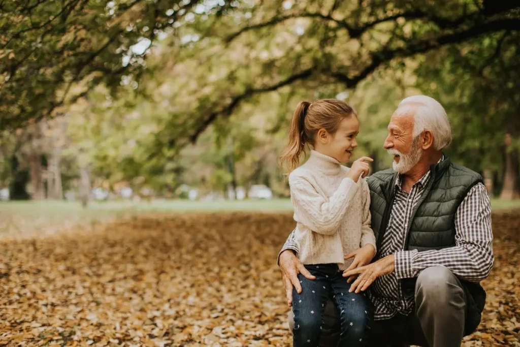 Older man and young girl smiling at each other in a park covered with autumn leaves