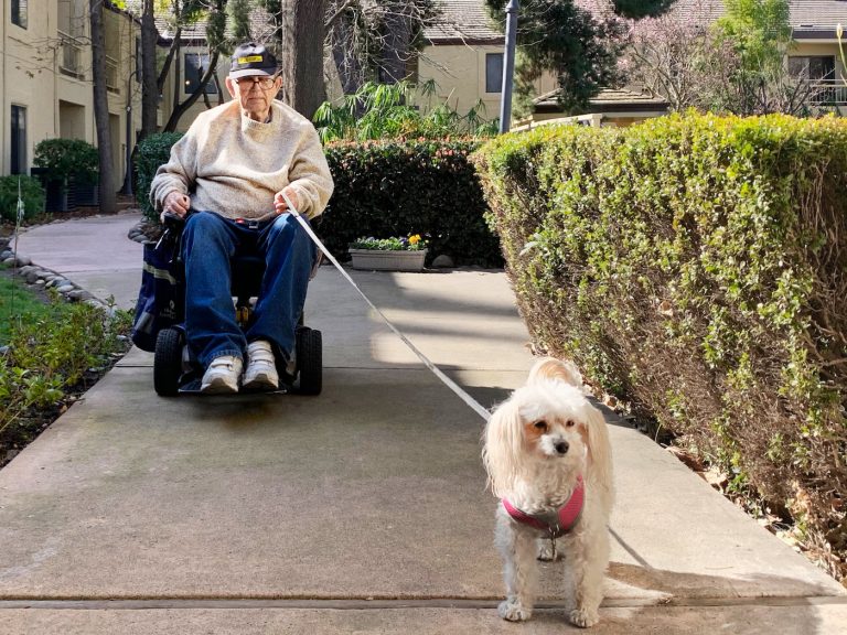 The Oaks at Inglewood | Resident riding across sidewalk with mobility scooter and dog