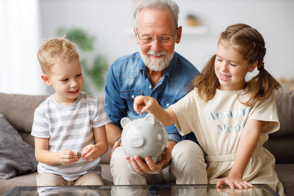 Pegasus Senior Living | Senior and his grand chi;den putting coins into a piggy bank