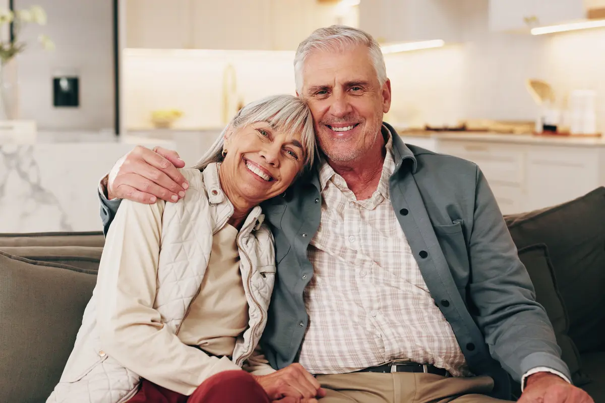senior couple smiling on a sofa, with the woman resting her head on the man’s shoulder and his arm around her