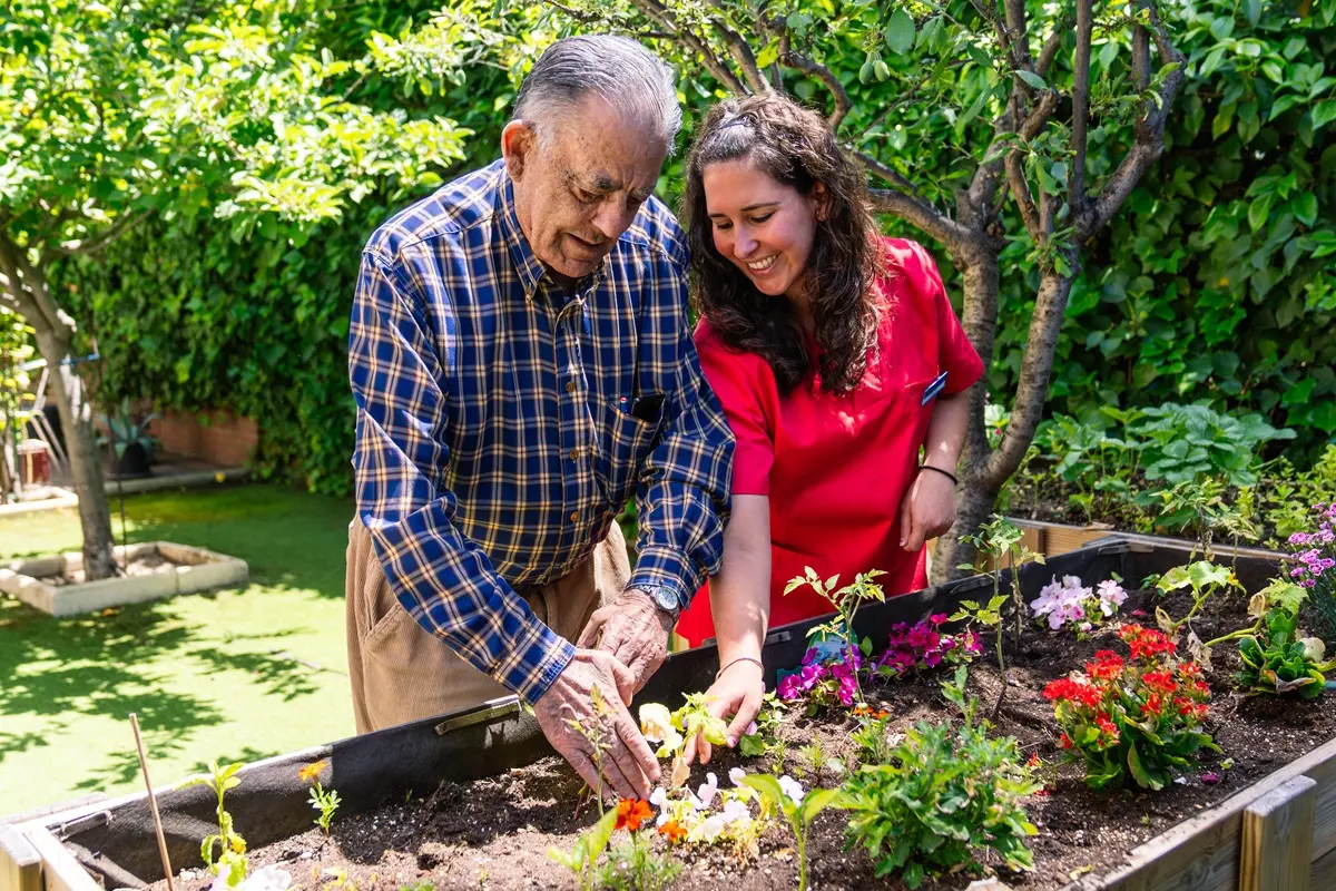 Senior and caregiver enjoying gardening in an outdoor raised bed.