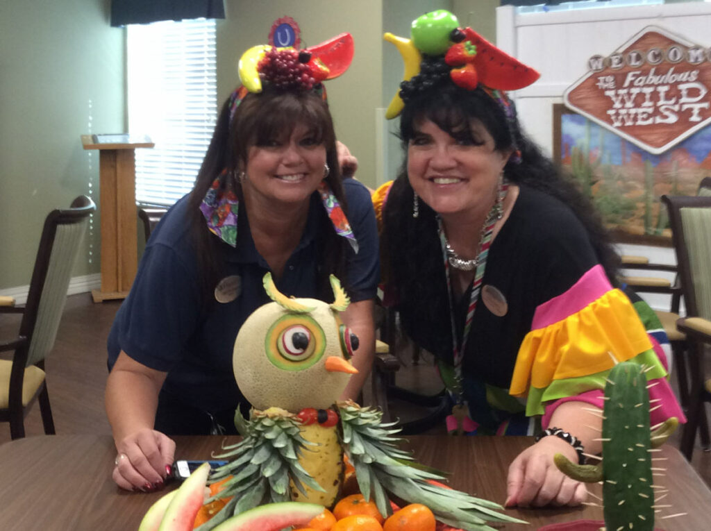 Broadway Mesa Village | Teresa Hadley smiling with her coworker behind sculpted fruit