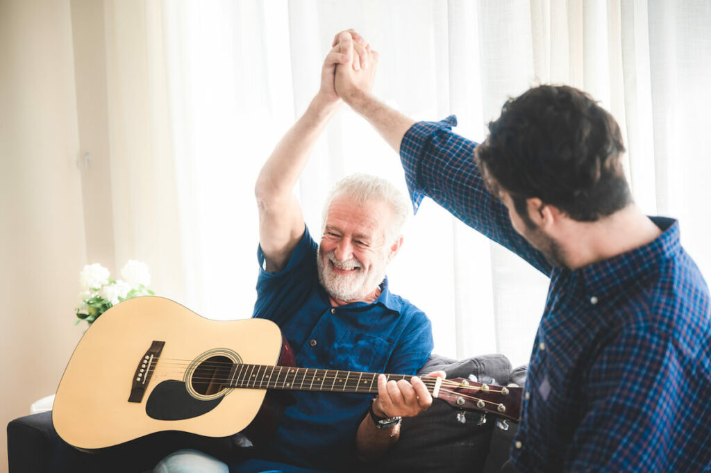 Pegasus Senior Living | Senior man holding a guitar and high-fiving his caregiver