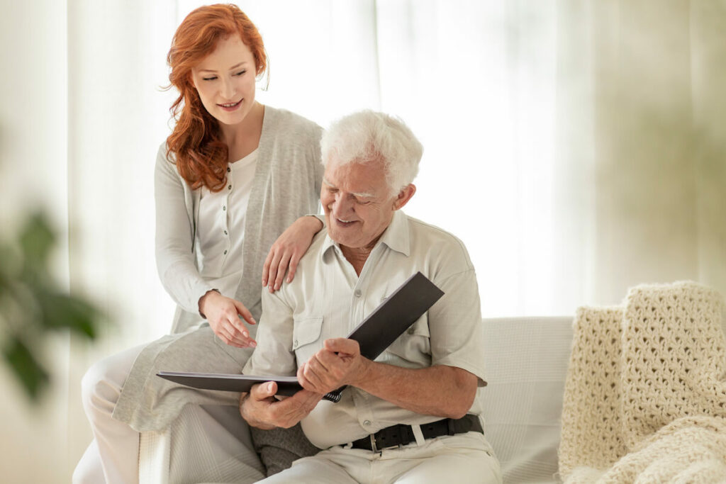 Cordata Court | Senior man looking at a photo album while sitting with his caretaker on the couch