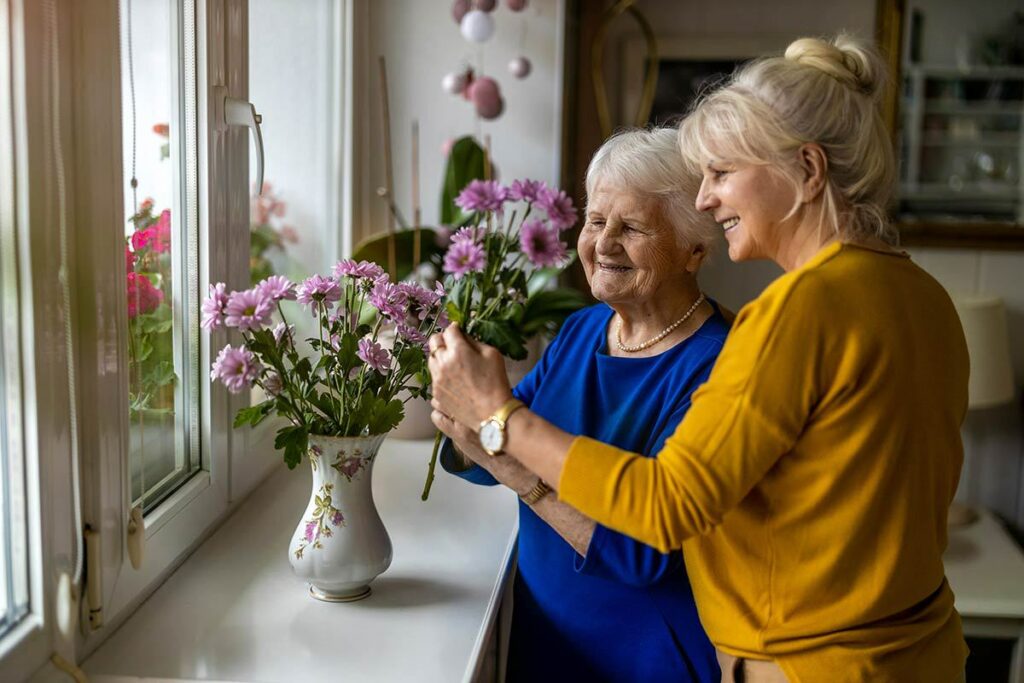 Cordata Court | Smiling senior woman with caregiver putting fresh flowers in a vase