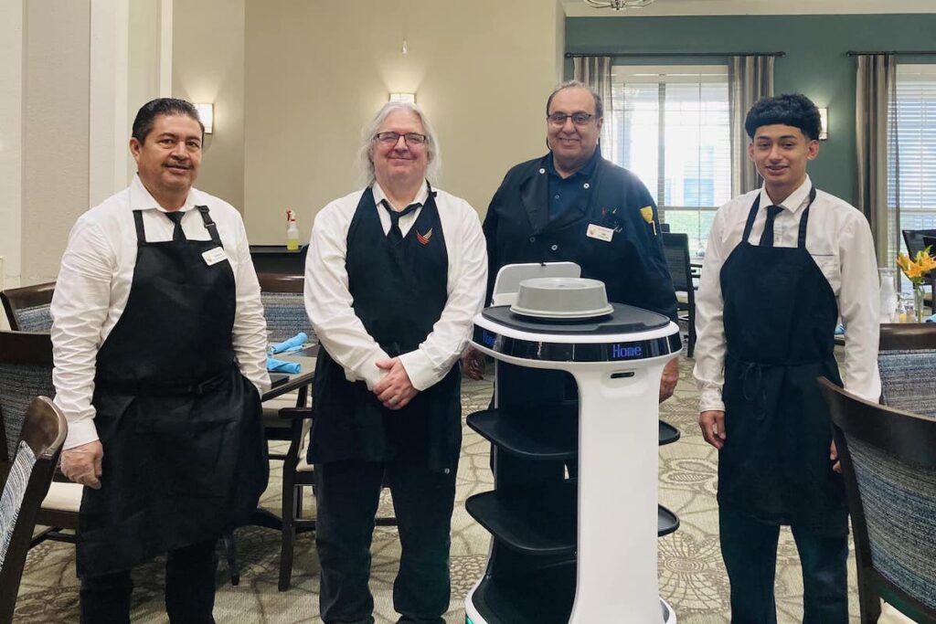 Town Village Crossing | The dining team standing next to a server robot
